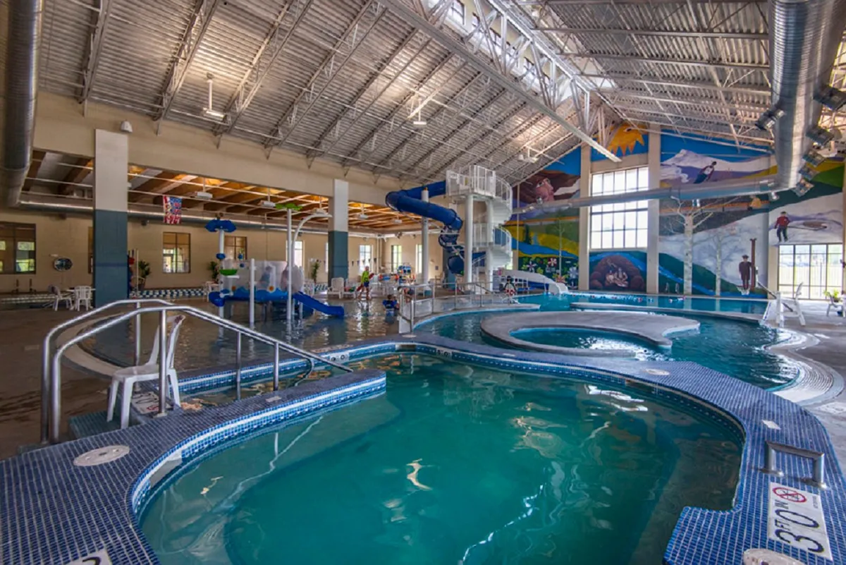A dynamic interior shot of the Grand Park Rec Center’s pool area, filled with children playing, colorful murals, water slides, and bright, inviting pools. The space is energetic, family-friendly, and clearly geared toward both fun and fitness for guests of all ages.