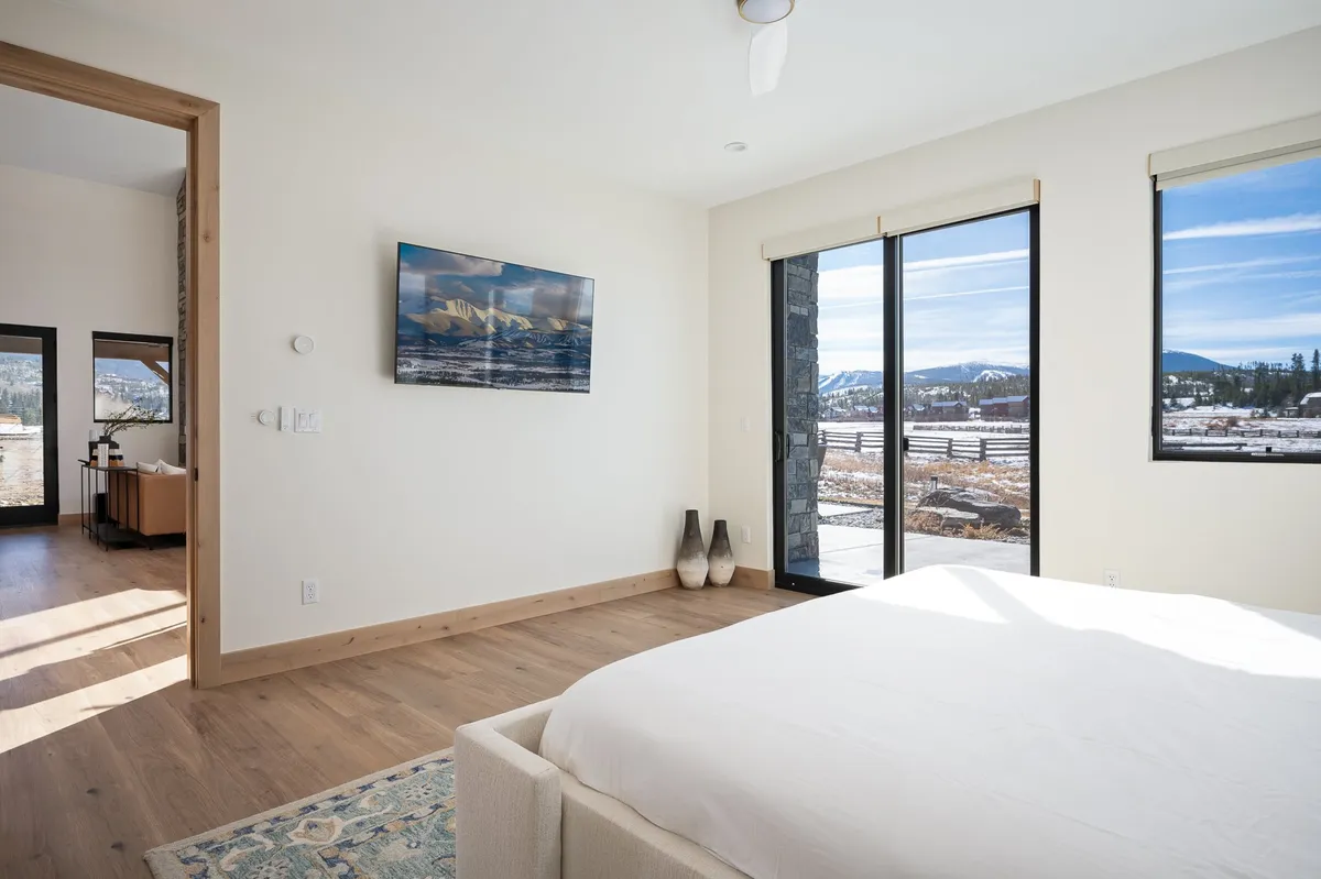 A minimalistic bedroom featuring a cozy bed against large windows with mountain views, tasteful wall art, and decorative vases. The natural light and calm design evoke a peaceful, private sanctuary.