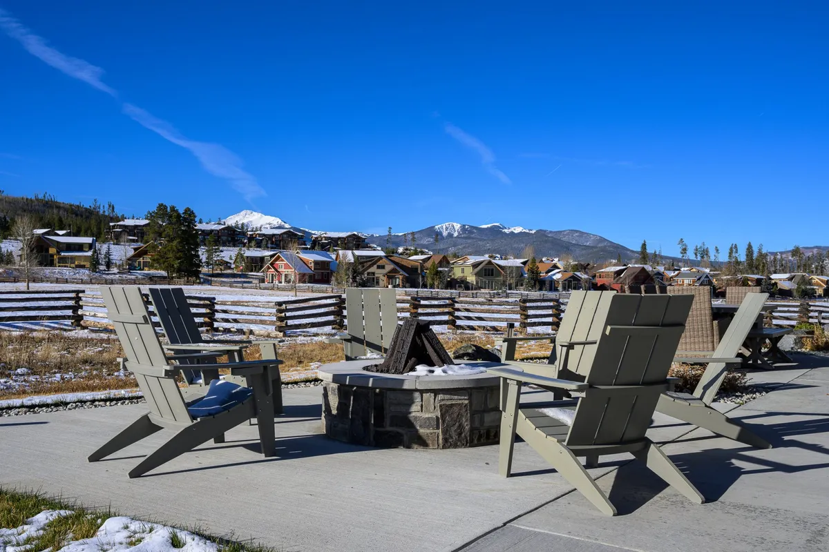 A cozy fire pit surrounded by adirondack chairs, with a snow-capped mountain vista in the background. The inviting arrangement encourages socializing and relaxation as the sun sets or under a starry sky.