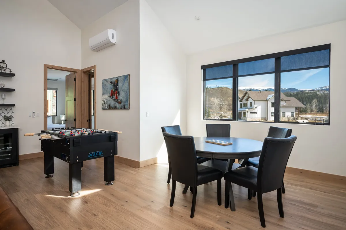 A lively game room scene with a foosball table positioned near a dining/game table and large windows letting in plenty of natural light. The setup exudes a playful, relaxed vibe ideal for friendly competition and group activities.