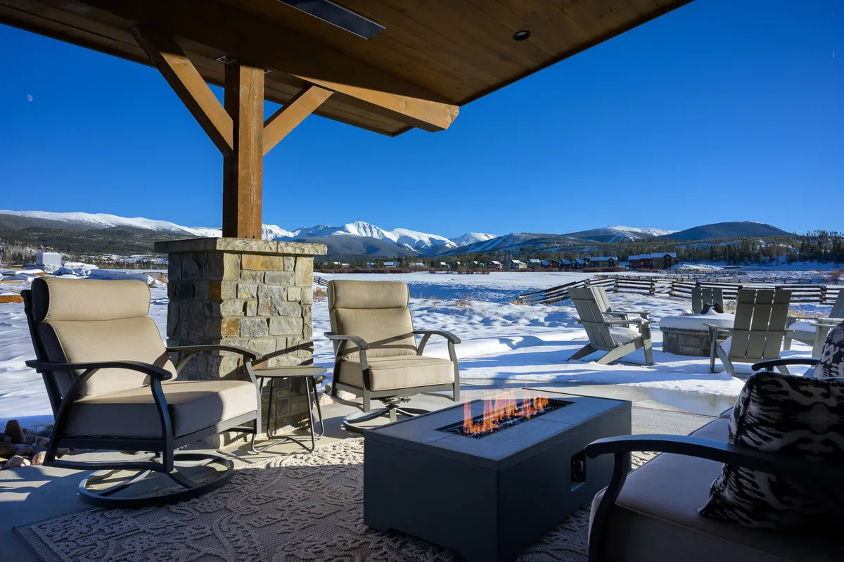 This exterior image captures a fire pit surrounded by rocking chairs, set against a snow-covered landscape with sweeping mountain views. The scene exudes warmth and tranquility, showing guests relaxing by the fire and socializing while enjoying natural beauty.