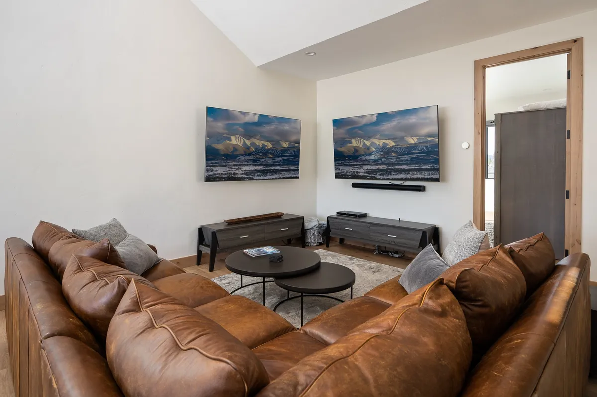 A modern entertainment loft featuring a leather sectional sofa arranged around two large flat-screen TVs. The space is cozy and inviting, ideal for movie marathons or gaming sessions with friends and family. Natural light brightens the room, enhancing its welcoming atmosphere.