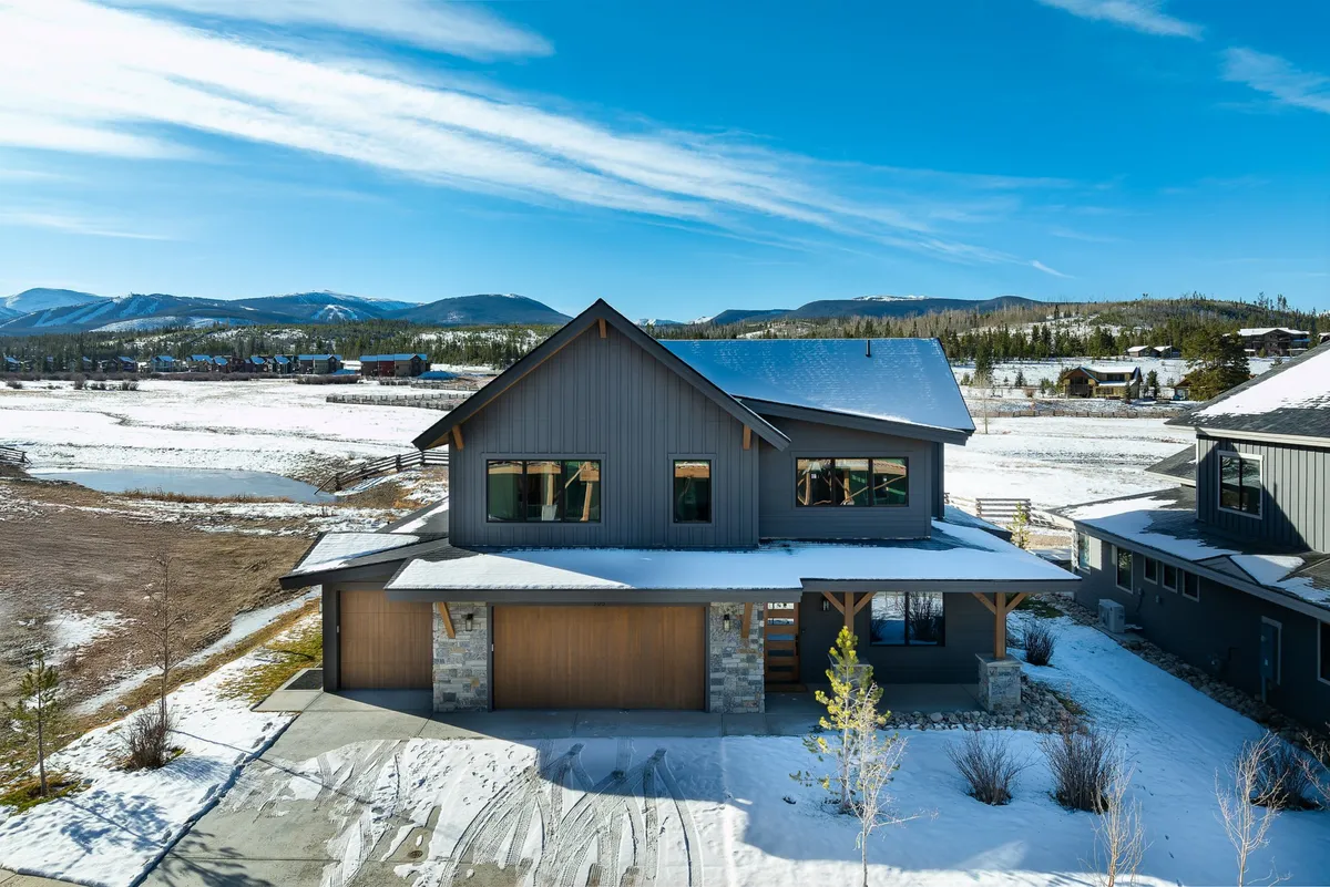 This image showcases the home's modern architectural exterior nestled within a snow-covered landscape, with a dramatic mountain backdrop. The inviting porch and clear views to the mountains emphasize a connection to the outdoors and local scenery.