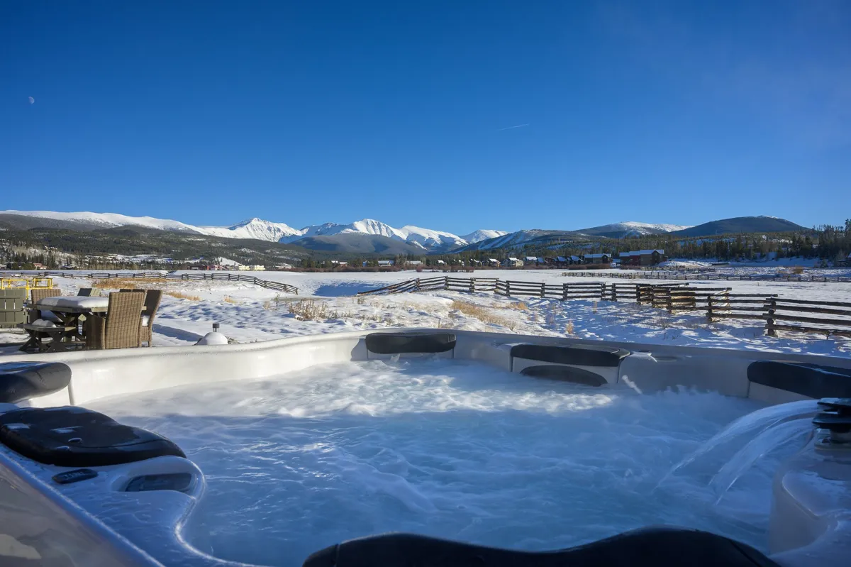 A tranquil exterior photo featuring a hot tub with a view of snow-capped mountains and an inviting outdoor seating area. The setting is peaceful, with opportunities for relaxation after a day of adventure, whether in winter or summer.